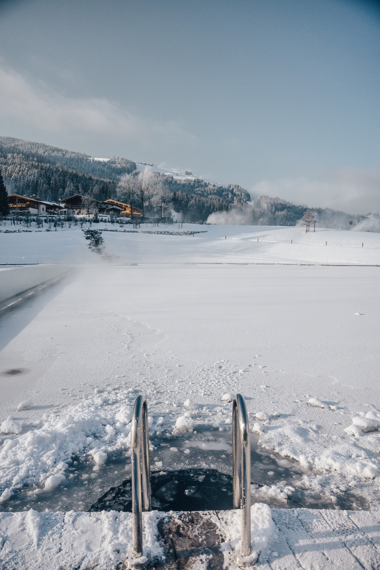 Verschneite Landschaft mit gefrorenem See und Leiter, im Hintergrund schneebedeckte Hügel